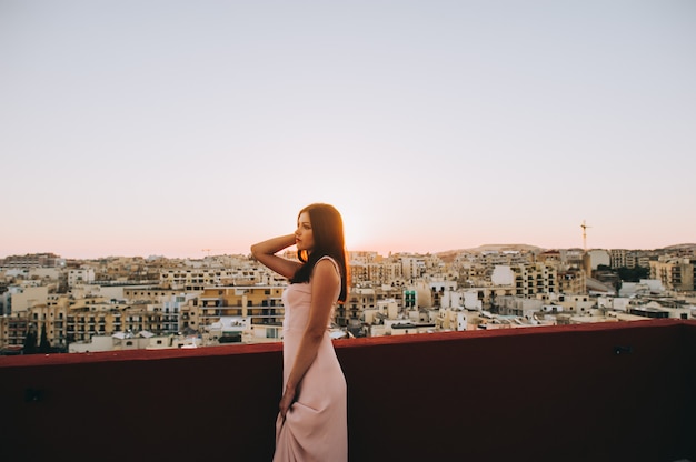 Bella giovane donna castana in un vestito da sera bianco. ambientazione sullo sfondo del tramonto della città.