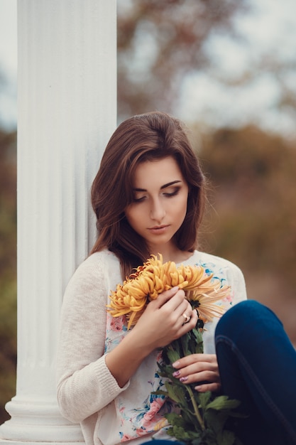 Bella giovane donna castana sorridente con i fiori nel parco di autunno