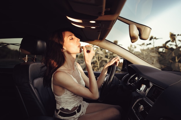 Bella giovane donna caucasica che dipinge le labbra sul sedile anteriore della sua auto