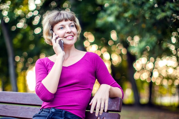 Bella giovane donna caucasica che utilizza il suo smartphone e che sorride nel parco