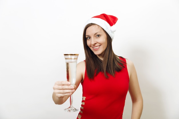 Bella giovane donna caucasica felice con un sorriso affascinante in abito rosso e cappello di Natale in piedi con un bicchiere di champagne su sfondo bianco. Ragazza di Santa isolata. Concetto di vacanza del nuovo anno 2018.