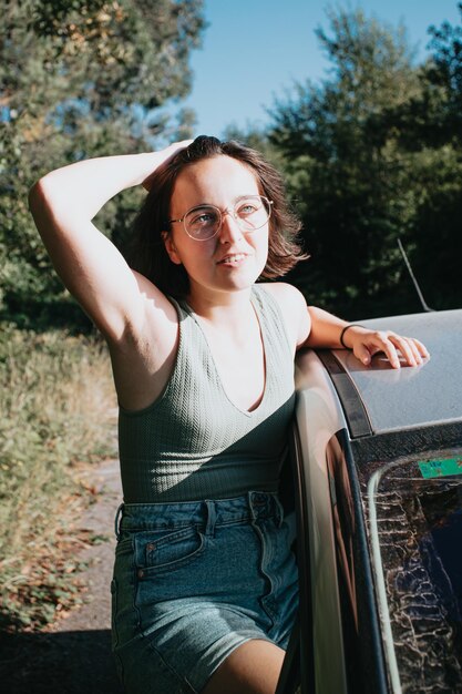 Bella giovane donna caucasica hipster in posa durante un viaggio in auto fuori dalla finestra. Stile di vita da furgone. Concetto di viaggio e felicità. Occhiali durante una giornata al tramonto