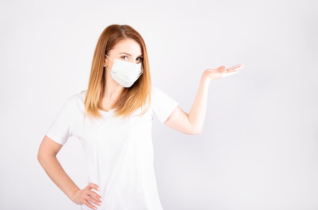 Bella giovane donna caucasica in maglietta bianca con maschera usa e getta. Protezione contro virus e infezioni.