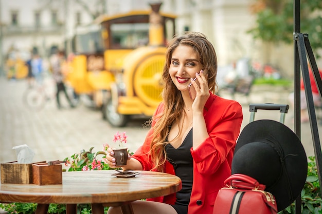 Bella giovane donna caucasica turistica parla al telefono seduto al tavolo in un caffè di strada in una città europea