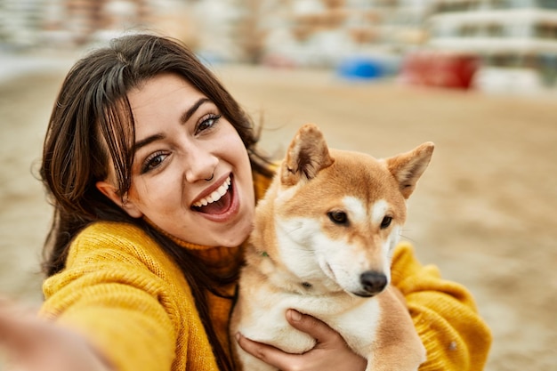 Bella giovane donna che abbraccia felice cane shiba inu in spiaggia