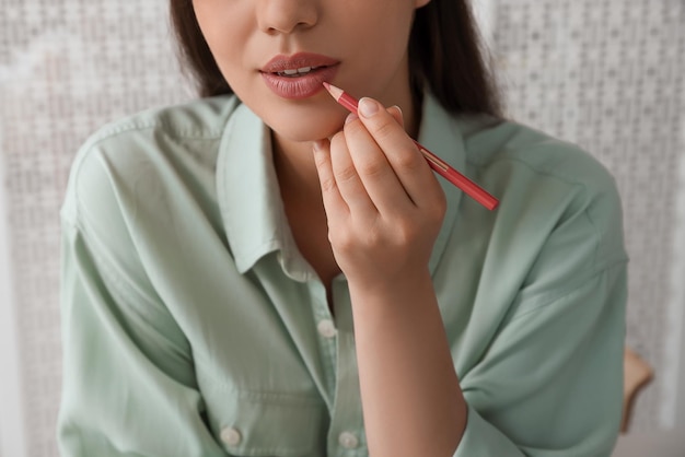 Bella giovane donna che applica la matita cosmetica sulle labbra al chiuso primo piano