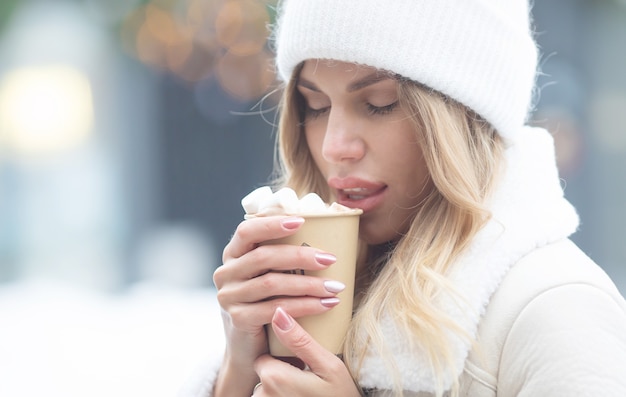 Bella giovane donna che beve cioccolata calda all'aperto. Natale.