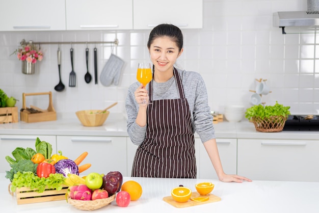 Bella giovane donna che beve succo d'arancia fresco in cucina. Dieta sana