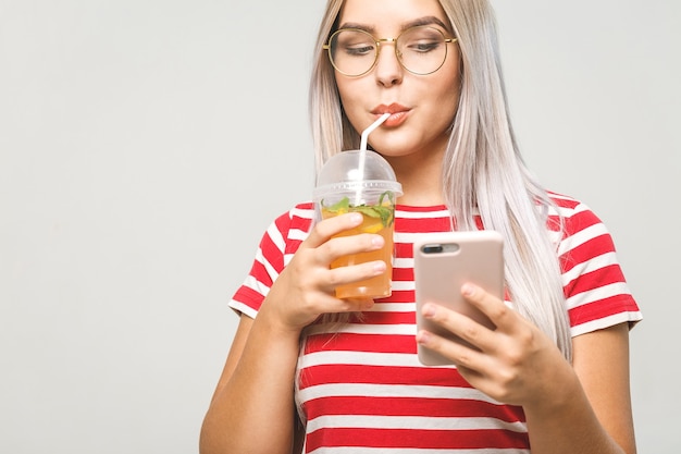 Bella giovane donna che beve un succo detox fatto in casa, mandando SMS sul suo telefono