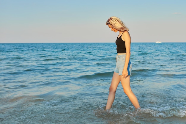 Bella giovane donna che cammina di profilo sull'acqua lungo la spiaggia del mare