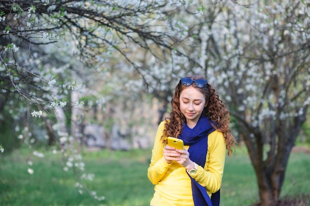 Bella giovane donna che cammina in primavera giardino con un telefono