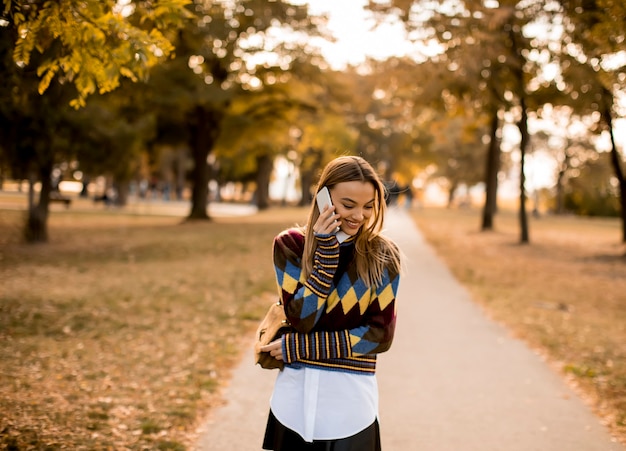 Bella giovane donna che cammina nel parco autunnale e usa un telefono cellulare