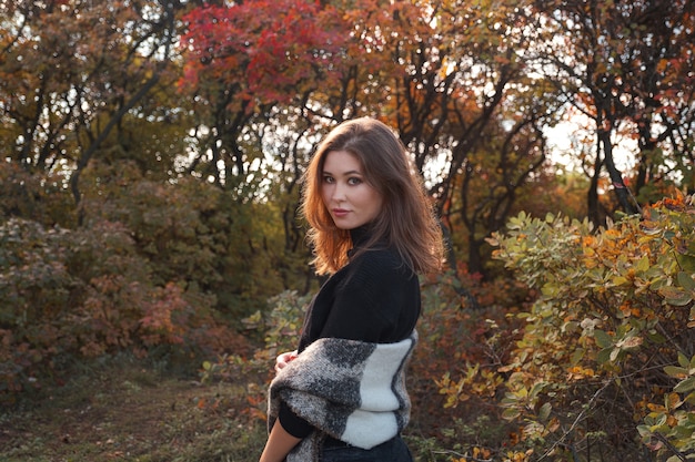 Bella giovane donna che cammina nella foresta di autunno. Tempo caldo e soleggiato