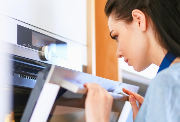 Bella giovane donna che controlla come sta andando la sua torta nel forno