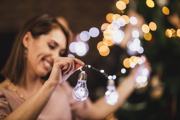 Bella giovane donna che decora la sua casa con le lampadine delle luci di Natale e si gode il tempo delle vacanze.