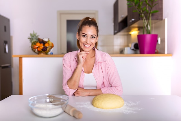 Bella giovane donna che esamina macchina fotografica e che sorride mentre cuocendo nella cucina a casa