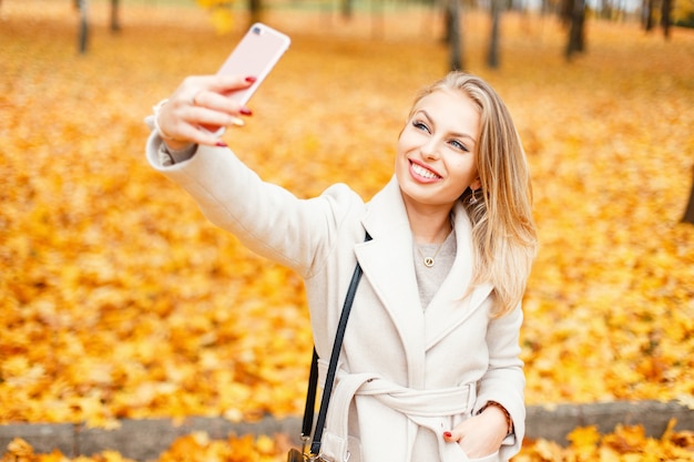Bella giovane donna che fa selfie su uno sfondo di fogliame di autunno giallo nel parco