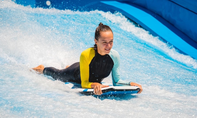 Bella giovane donna che fa surf su un simulatore di onde in un parco divertimenti acquatico