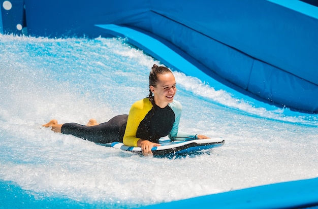 Bella giovane donna che fa surf su un simulatore di onde in un parco divertimenti acquatico