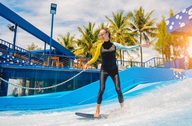 Bella giovane donna che fa surf su un simulatore di onde in un parco divertimenti acquatico