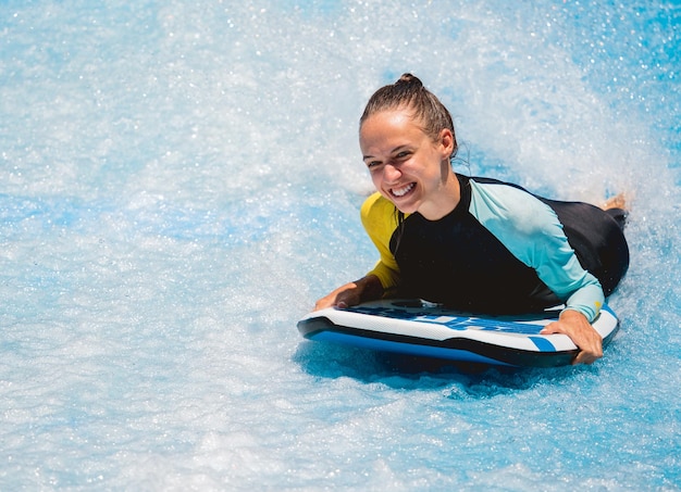 Bella giovane donna che fa surf su un simulatore di onde in un parco divertimenti acquatico