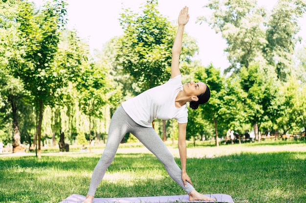 Bella giovane donna che fa yoga al parco e distoglie lo sguardo. Donna castana che si gode la natura durante un esercizio di respirazione