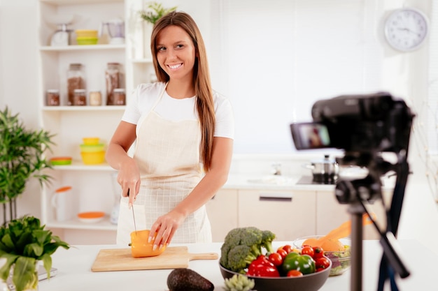 Bella giovane donna che filma la sua trasmissione sul blog sul cibo sano a casa.