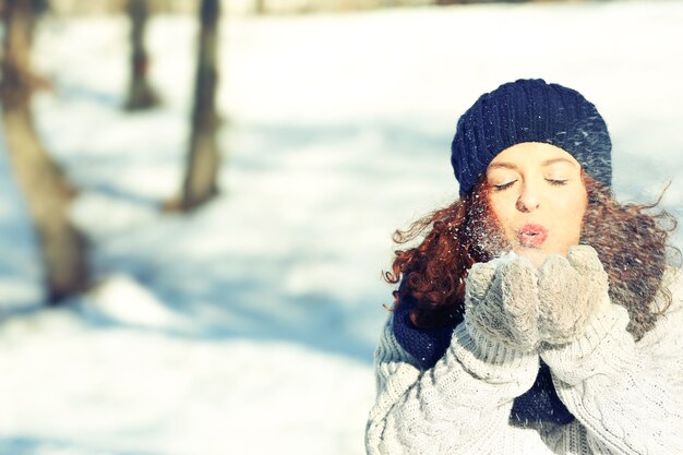 Bella giovane donna che gioca con la neve all'aperto il giorno d'inverno