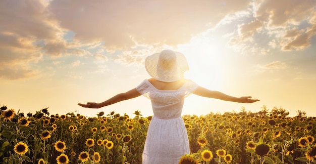 Bella giovane donna che gode della natura sul campo dei girasoli al tramonto