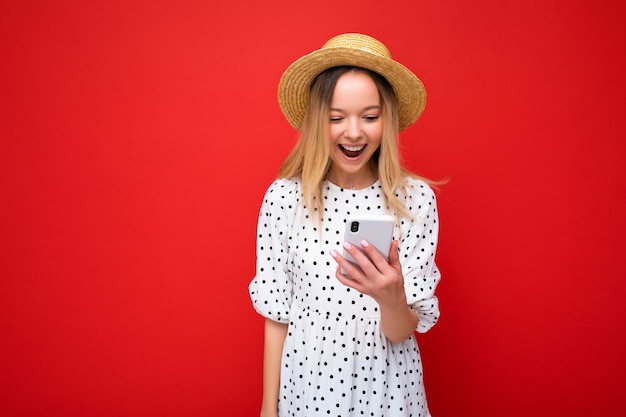 Bella giovane donna che indossa abiti casual in piedi isolato su sfondo navigazione su Internet tramite telefono guardando lo schermo del cellulare.