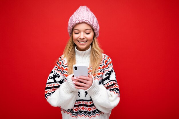 Bella giovane donna che indossa abiti casual in piedi isolato su sfondo navigazione su Internet tramite telefono guardando lo schermo del cellulare.