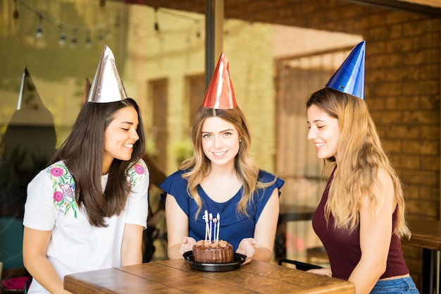 Bella giovane donna che indossa cappelli da festa che celebra il suo compleanno con gli amici in un ristorante