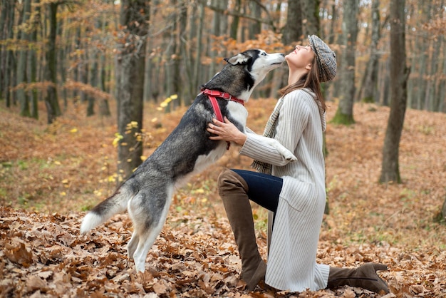 Bella giovane donna che indossa cappello e maglione che bacia la sua ragazza cane con il suo animale domestico che si rilassa fuori dall'autunno