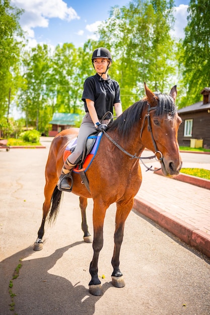 Bella giovane donna che indossa il casco in sella al suo cavallo marrone