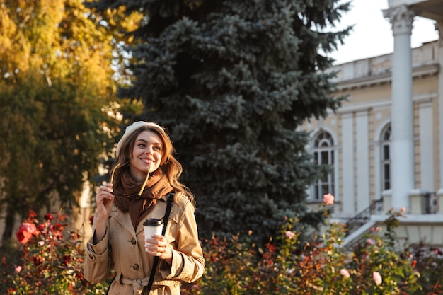 Bella giovane donna che indossa un cappotto che cammina all'aperto, bevendo caffè