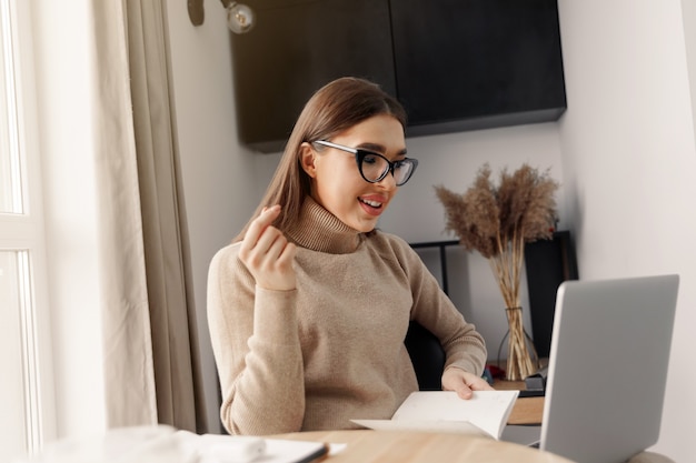 Bella giovane donna che lavora al computer portatile mentre era seduto in soggiorno, bevendo caffè. Ministero degli interni durante la quarantena di Coronavirus o Covid-19.