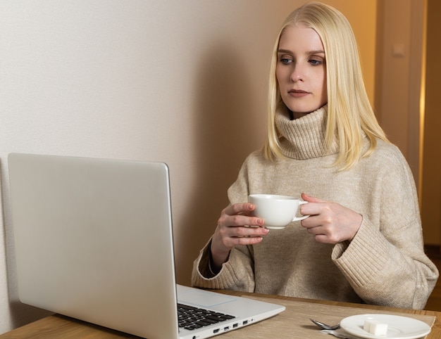 Bella giovane donna che lavora al computer portatile mentre era seduto in soggiorno, bevendo caffè.