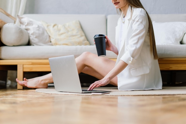 Bella giovane donna che lavora al computer portatile mentre era seduto in soggiorno, bevendo caffè