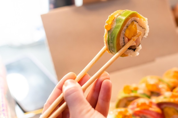 Bella giovane donna che mangia il rotolo di sushi al caffè. Donna che mangia sushi con le bacchette sul ristorante.