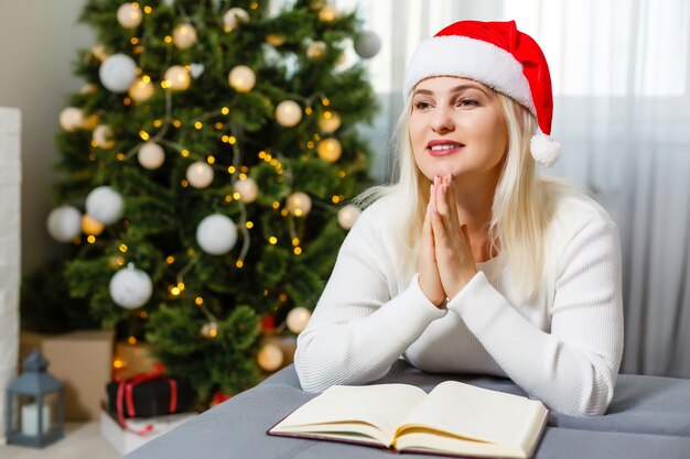 Bella giovane donna che prega davanti all'albero di Natale decorato