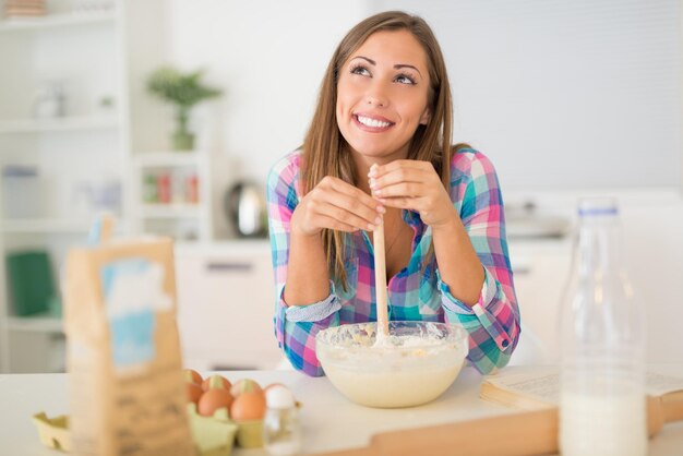 Bella giovane donna che produce pasta nella cucina domestica.