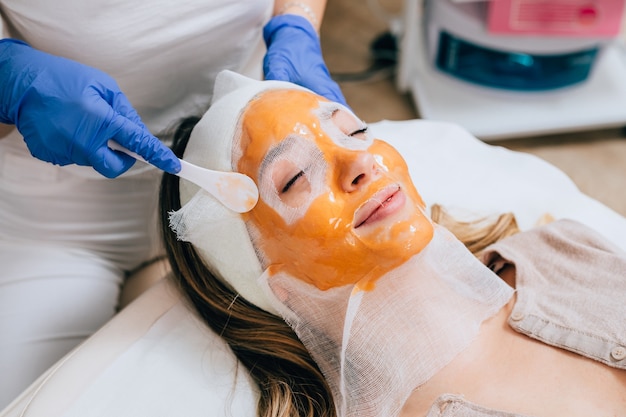 Bella giovane donna che riceve maschera facciale con effetti ringiovanenti nel salone di bellezza della stazione termale.