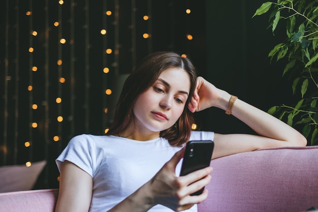 Bella giovane donna che riposa su un divano e utilizzando il telefono cellulare