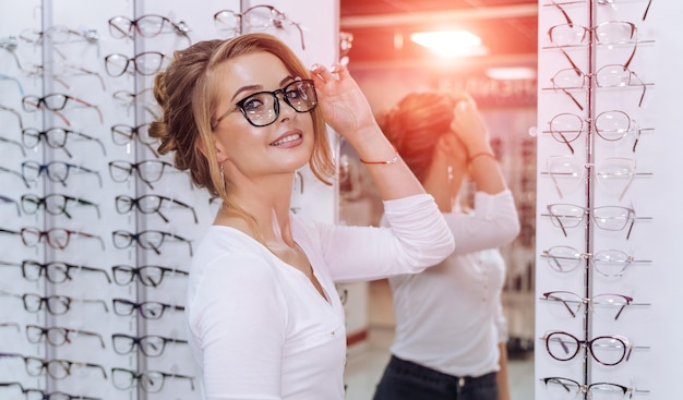 Bella giovane donna che sceglie un nuovo paio di occhiali nel negozio di ottica Correzione della vista Ottica Oftalmologia