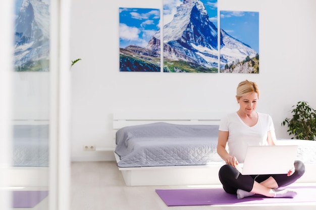 Bella giovane donna che si allena online a casa sul computer portatile, copia dello spazio. Ritratto a figura intera. Yoga, pilates, esercizio fisico