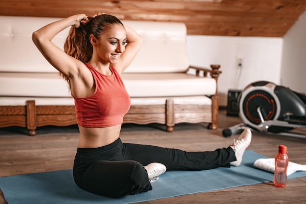 Bella giovane donna che si prepara per l'allenamento a casa. Si lega i capelli in una coda di cavallo e fa esercizi di stretching.