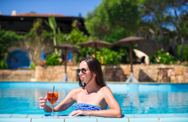 Bella giovane donna che si rilassa nella piscina con il cocktail saporito