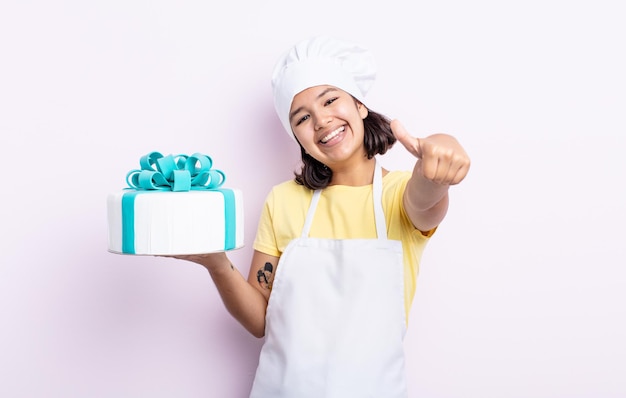 Bella giovane donna che si sente orgogliosa, sorride positivamente con i pollici in su. chef che cucina una torta