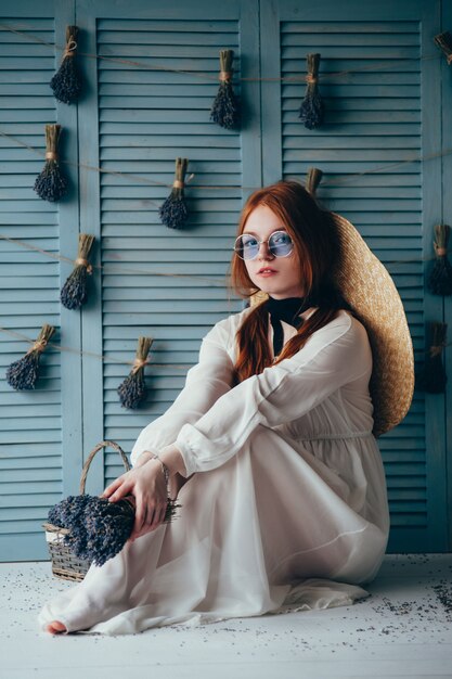 Bella giovane donna che si siede con la lavanda contro la parete blu.