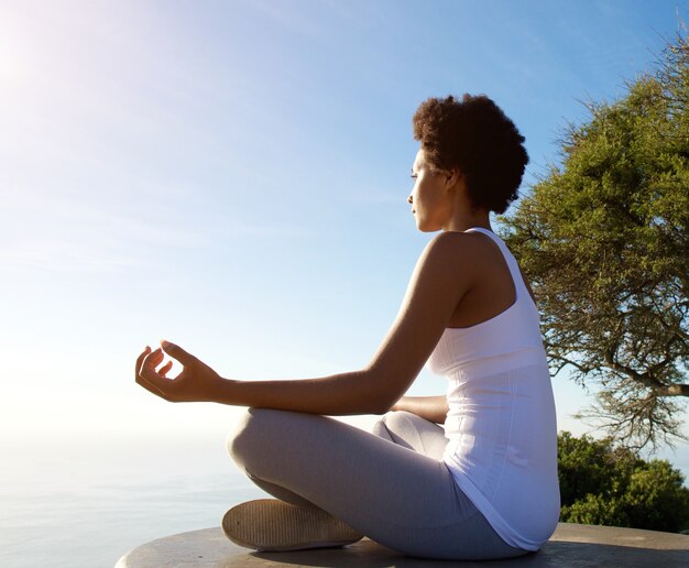 Bella giovane donna che si siede nella posa di yoga in spiaggia